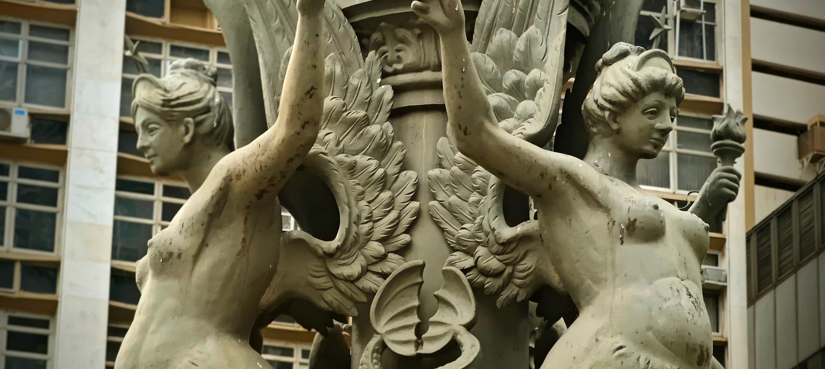 Two sculpted female figures flank ornate architectural stonework on a central Rio building.