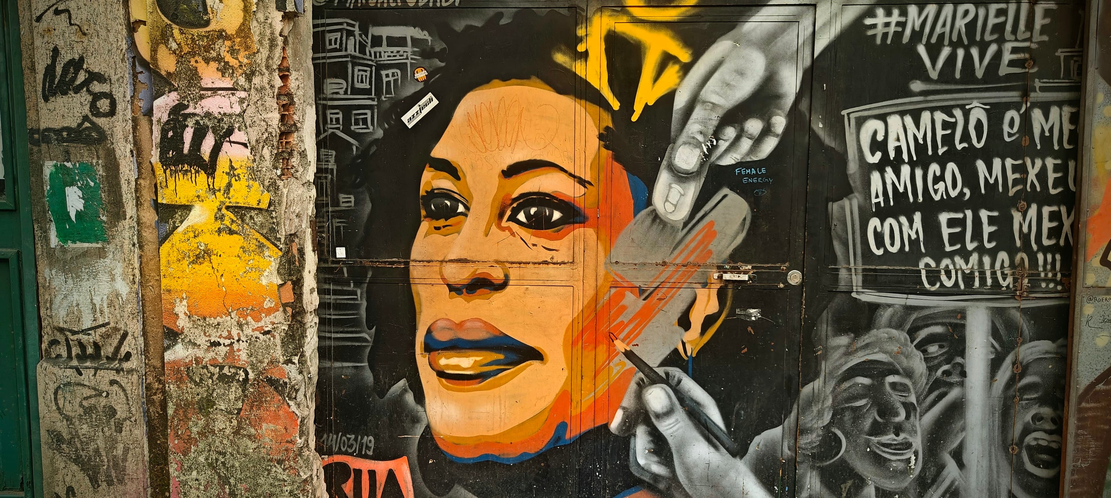 A painted portrait of a woman appears beside the words Marielle Vive on a wall in central Rio.