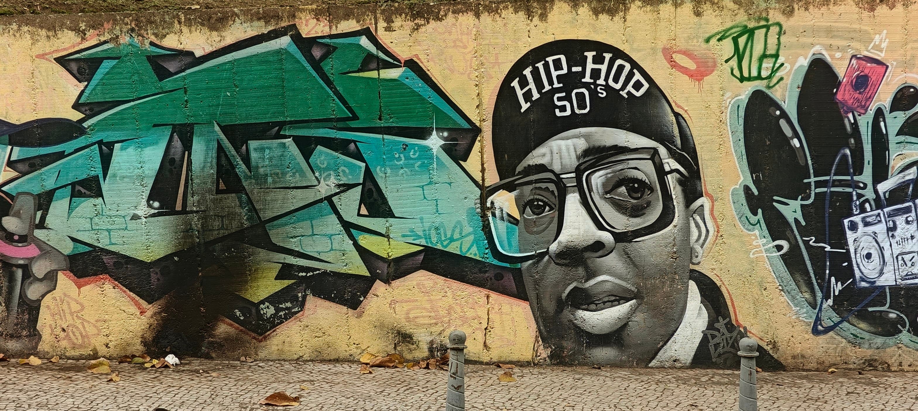 A large black-and-white portrait in a cap is painted beside colourful graffiti in Lapa.