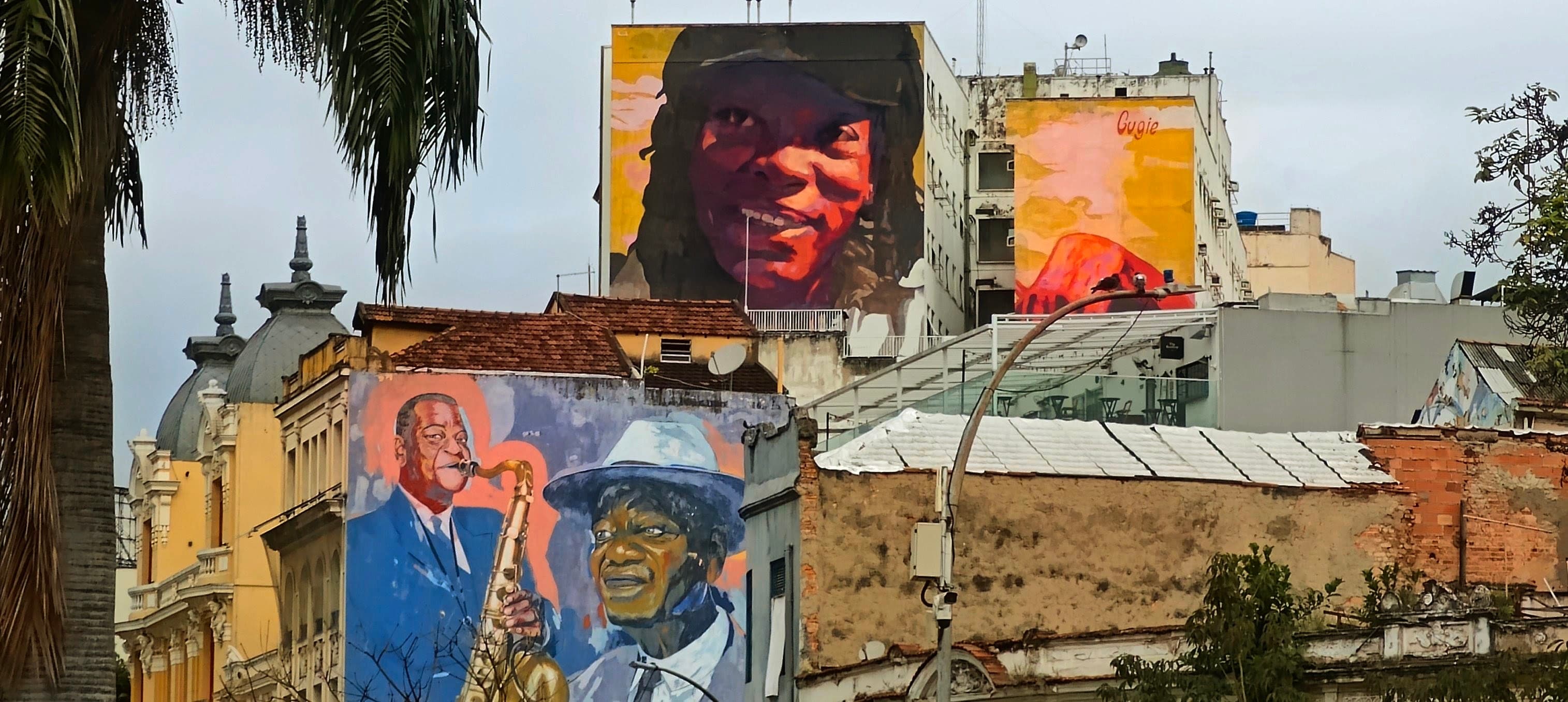 Large colourful murals with faces and musicians rise above low buildings in Lapa.