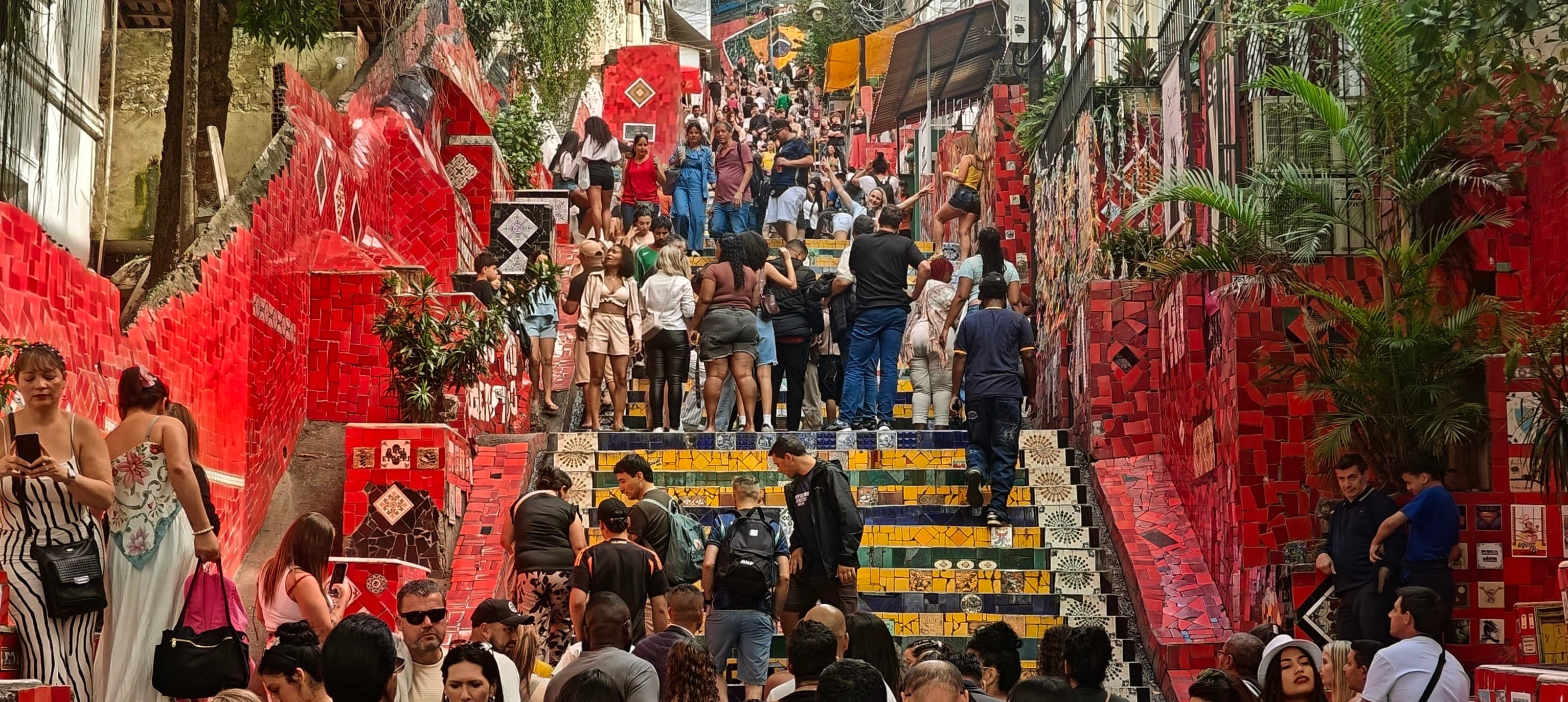 Visitors crowd the colourful tiled Escadaria Selarón between red-painted walls.