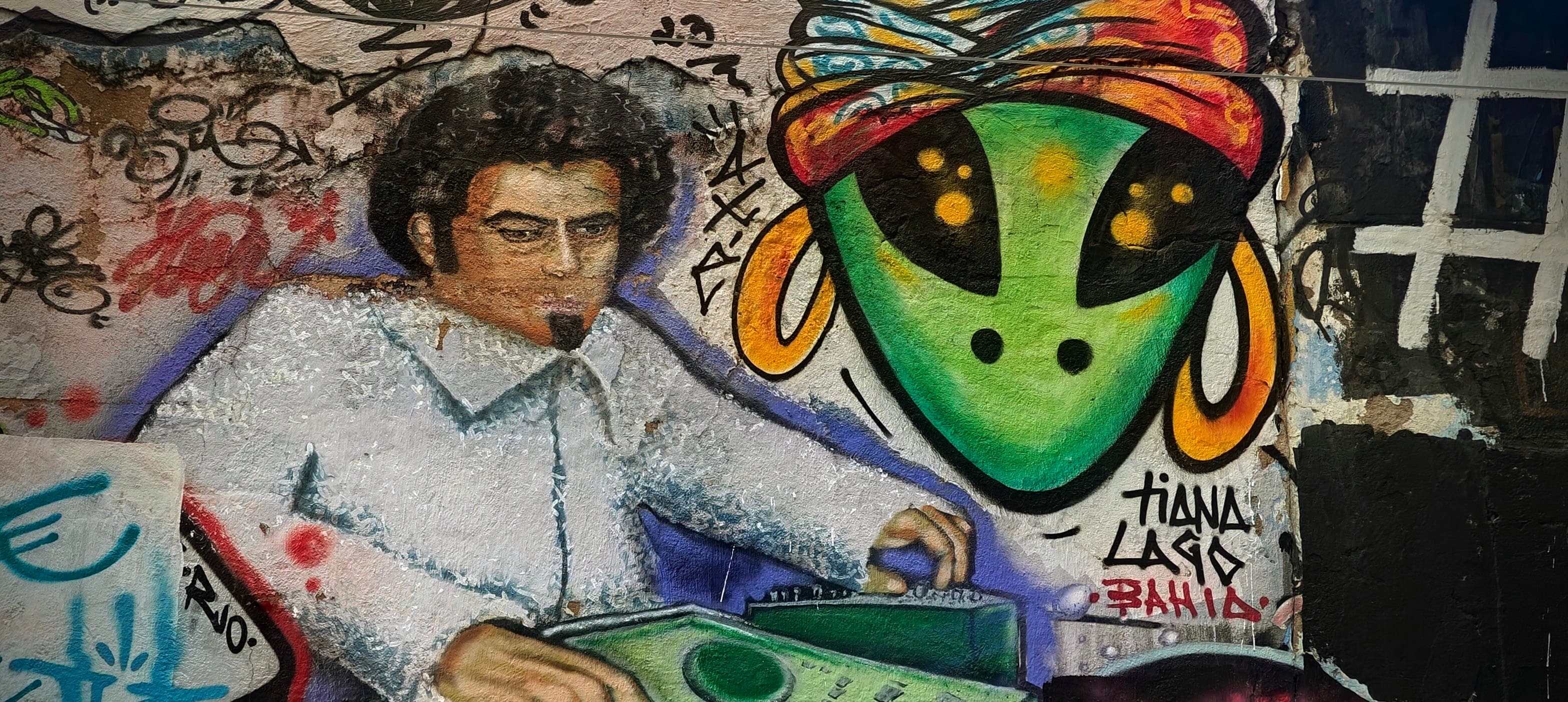 A painted portrait and a green alien face cover a graffiti wall in Rio de Janeiro.