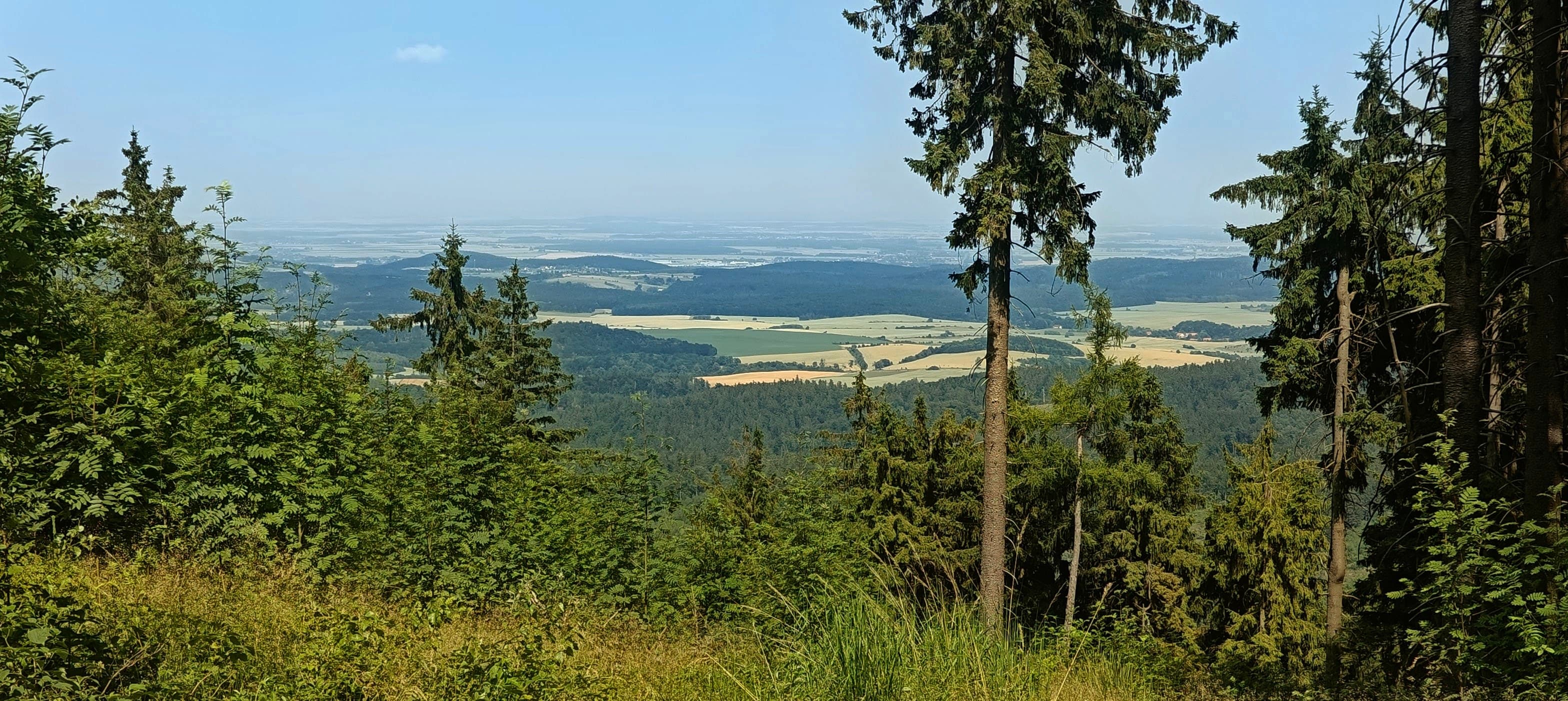 View through trees from Trójgarb toward patchwork fields and distant lowlands.