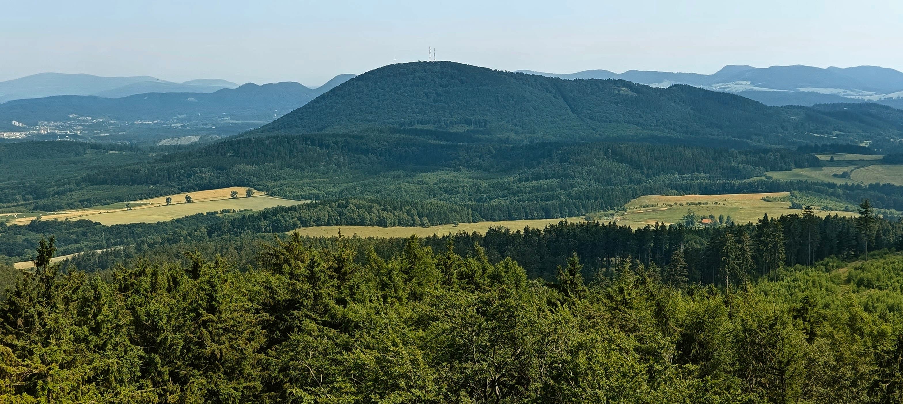 Rounded forested mountain with a summit structure seen from Trójgarb above fields and woodland.