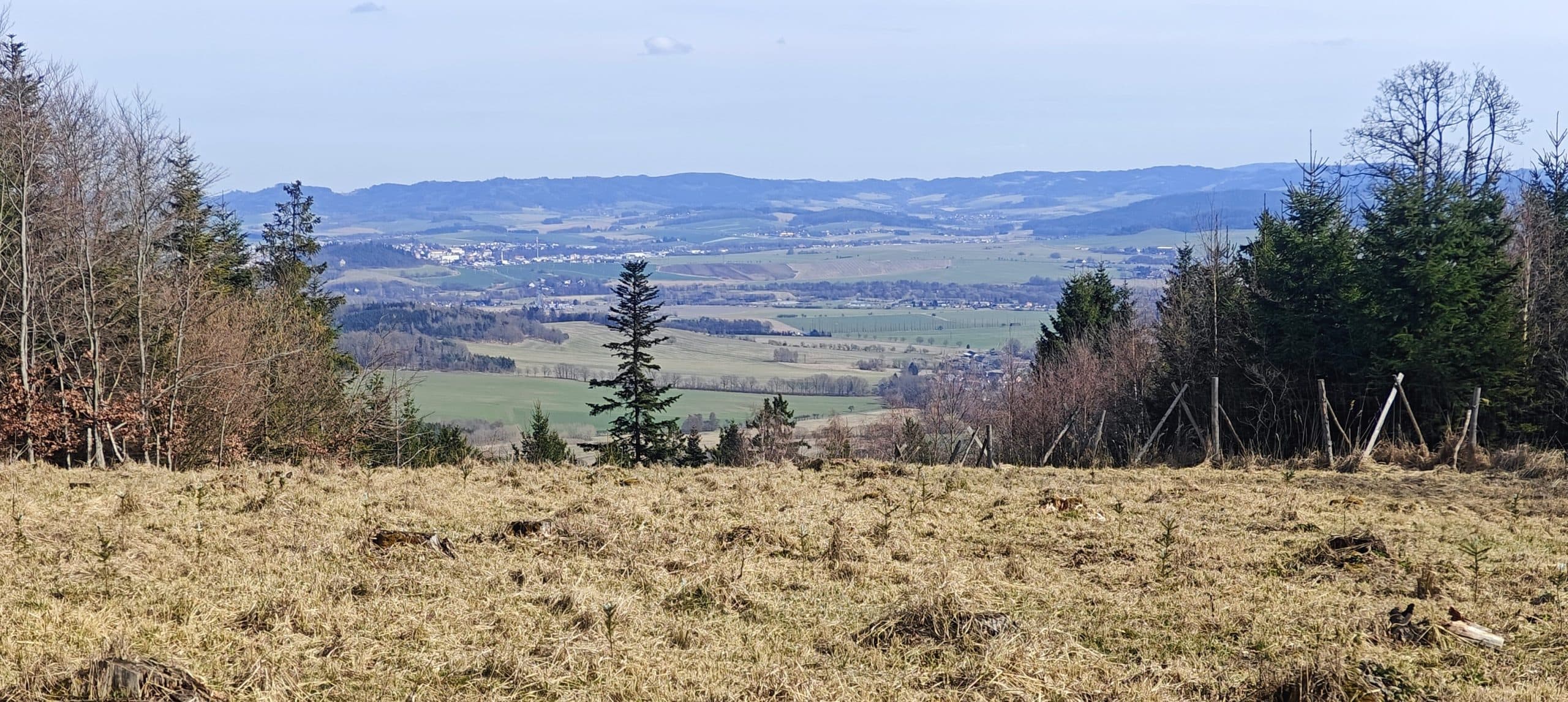 View from a grassy logged clearing across fields, villages and low wooded ridges.
