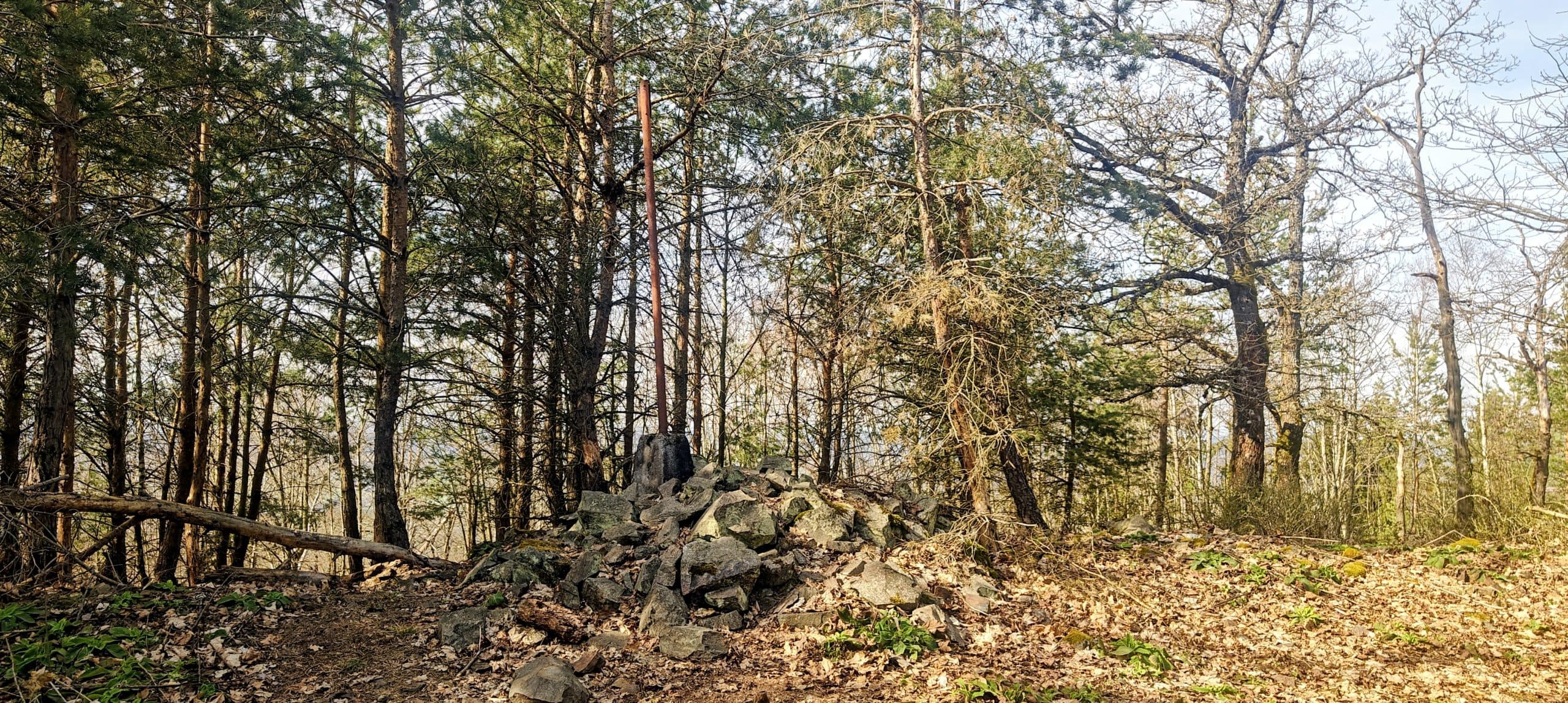 Rusty metal triangulation post rising from a collapsed stone pile in the forest.