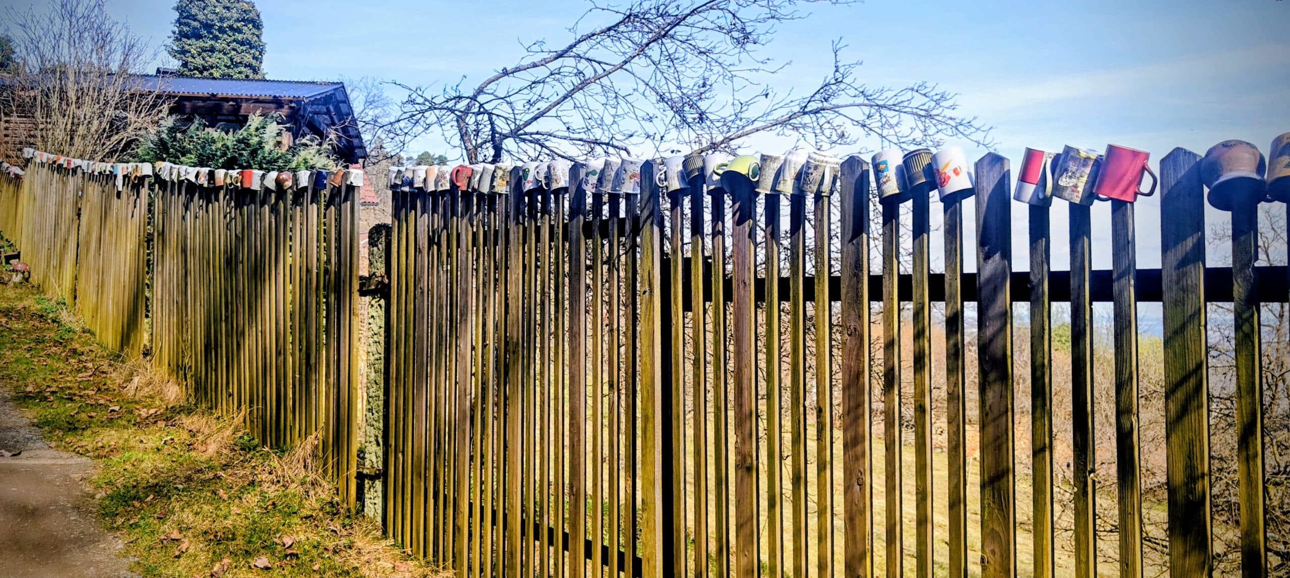 Wooden fence in Struhadlo with assorted mugs lined along the top.