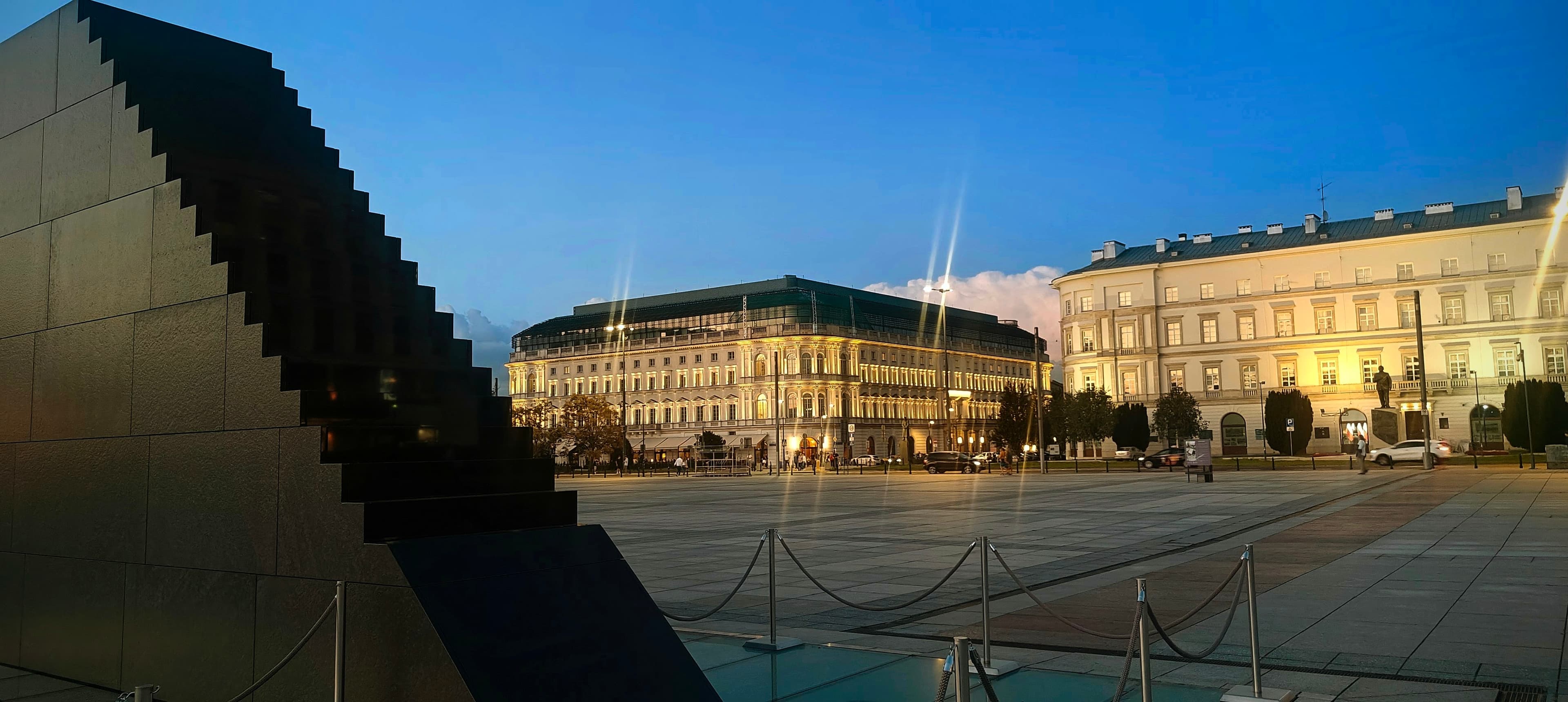 Black Smolensk memorial in central Warsaw at blue hour, with the open ceremonial square behind it.