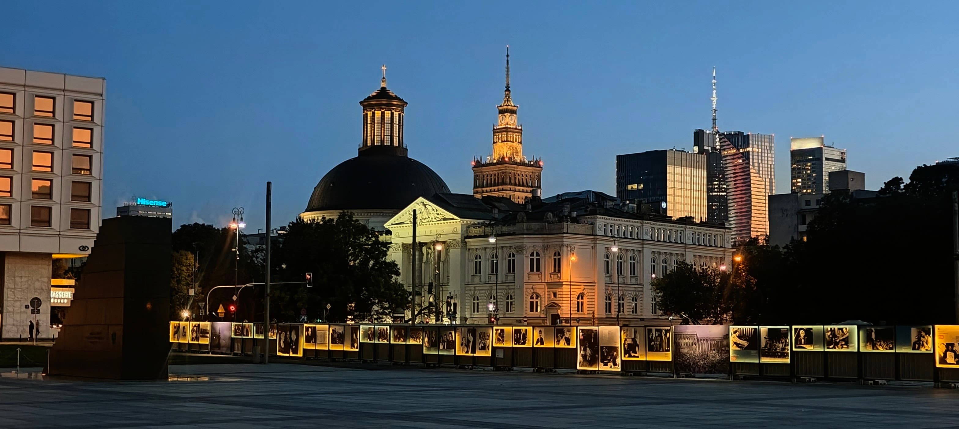 Warsaw city-centre skyline at dusk with the dome of Holy Trinity Church and illuminated buildings.