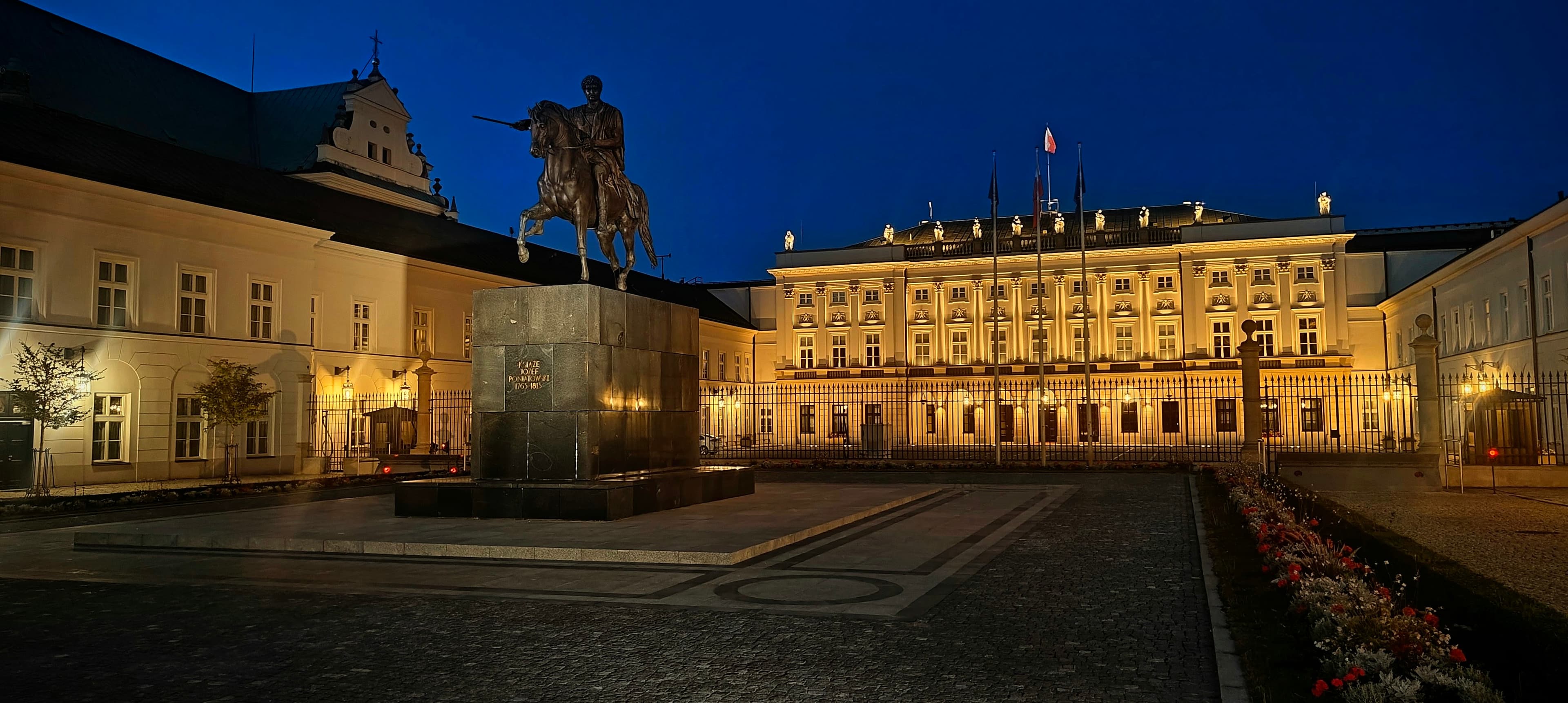 Presidential Palace in Warsaw illuminated at night with an equestrian statue in the foreground.
