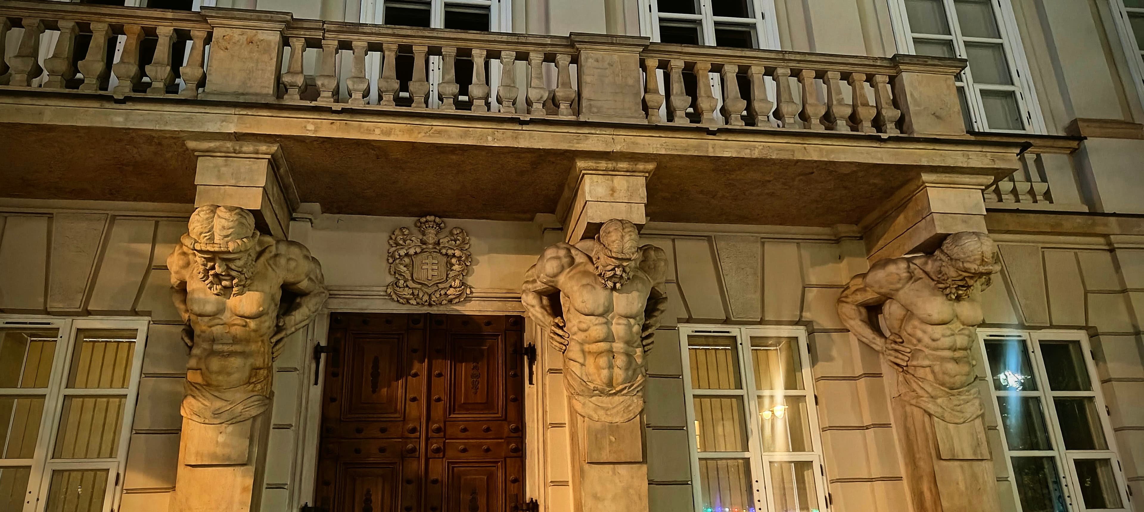 Four stone Atlantes supporting a balcony above the entrance of the Tyszkiewicz-Potocki Palace.