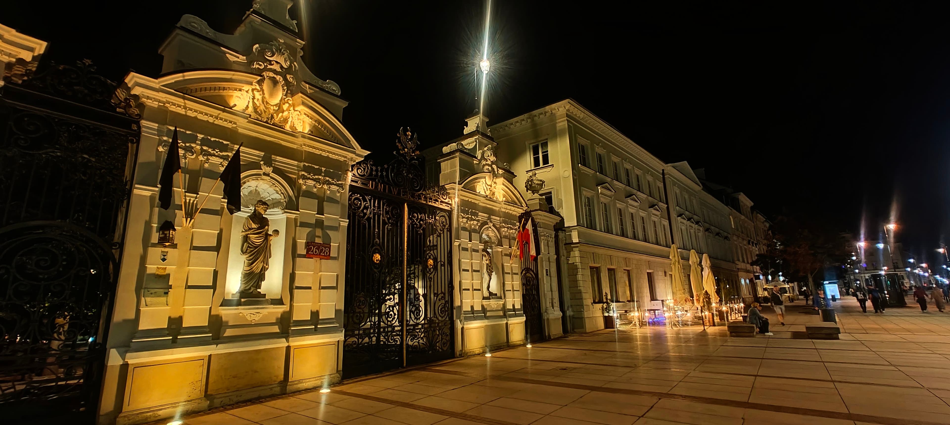 Illuminated University of Warsaw main gate on Krakowskie Przedmieście at night.