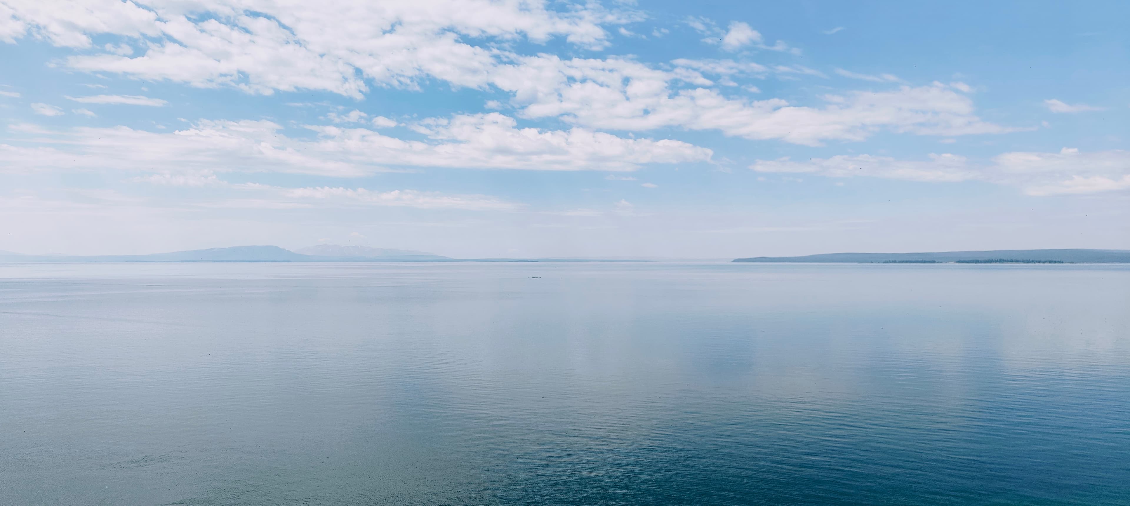 Wide blue water on Yellowstone Lake beneath broken clouds and distant low mountains.