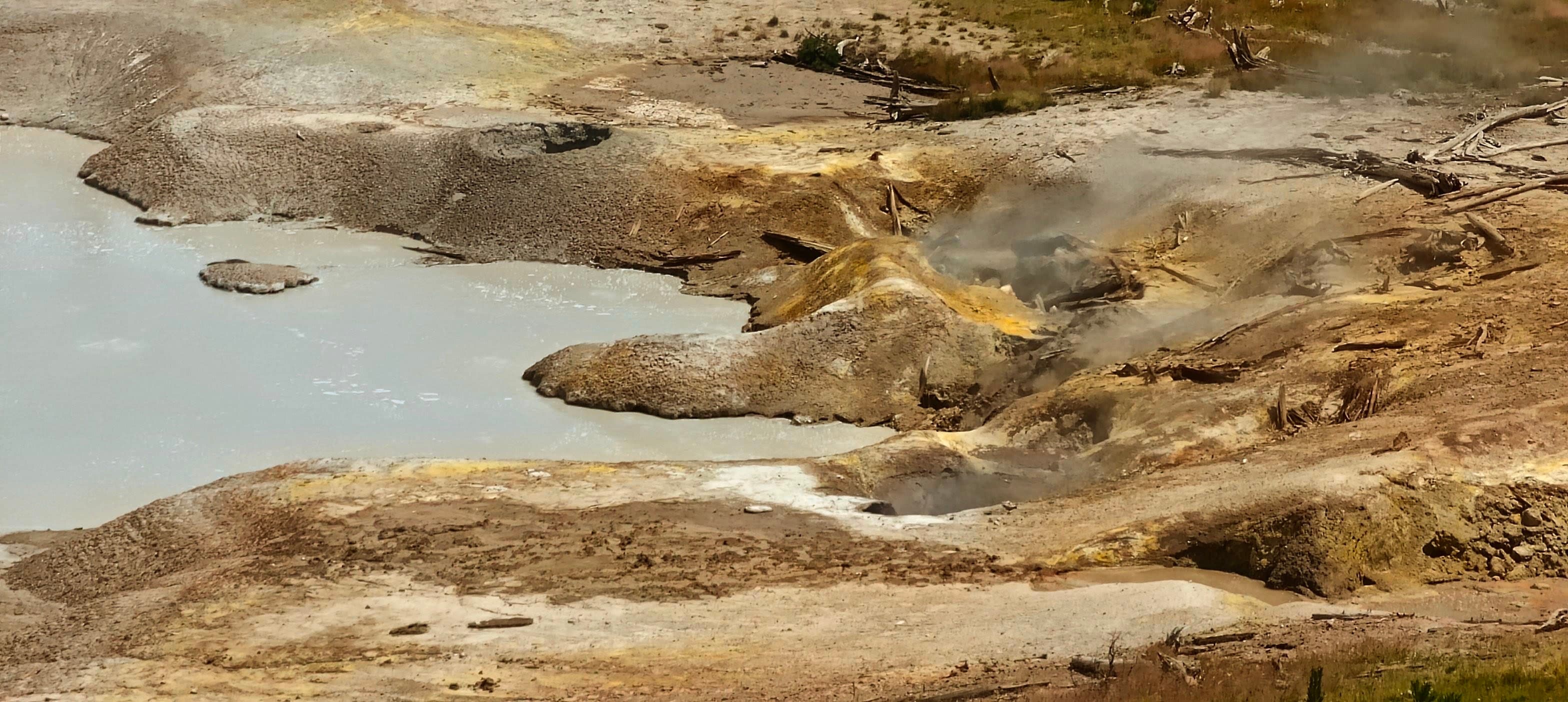 Ochre mineral channels and grey mudpots spread across pale geothermal ground.