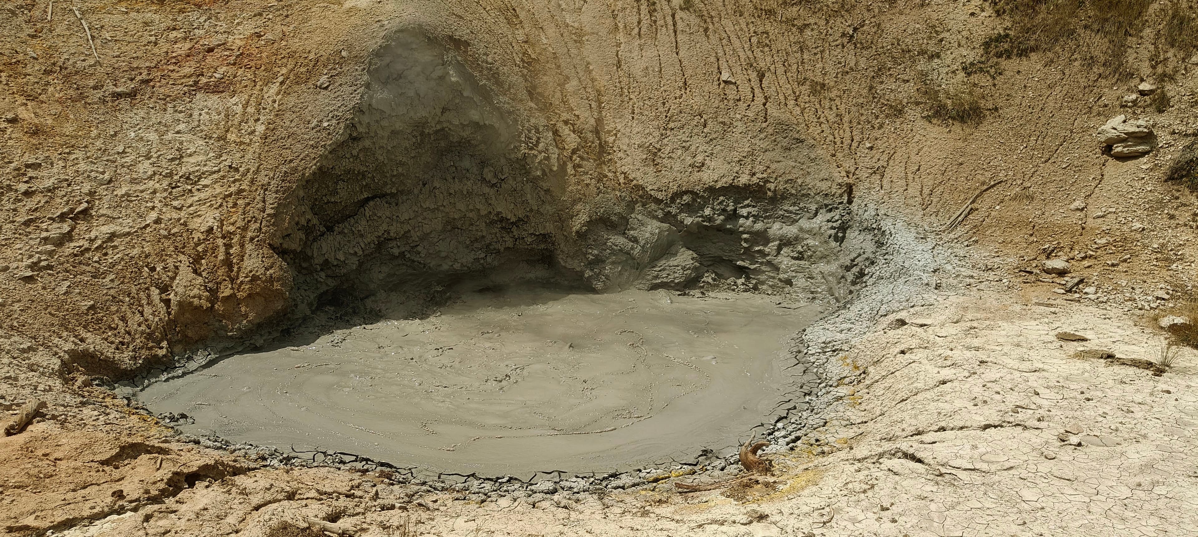 Thick grey mud bubbles inside a steep-sided geothermal depression.