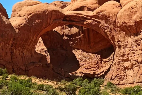 Large red sandstone arch above shrubs and broken rock in Arches National Park.