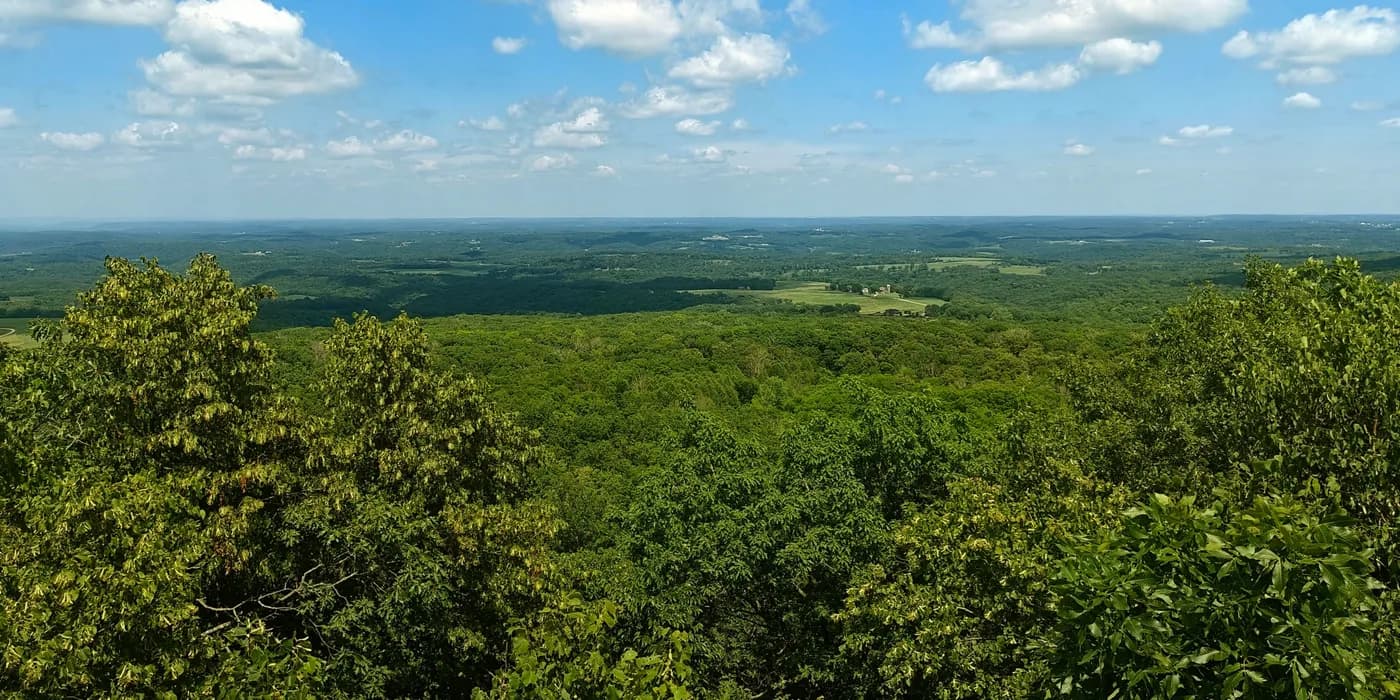 Wide view over forest, farmland and low ridges under a blue sky from an observation tower at Blue Mound.