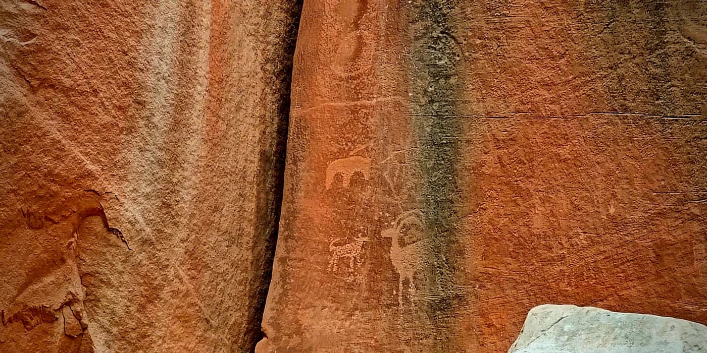 Faint Fremont Culture petroglyph figures visible in darker desert varnish along a narrow sandstone seam.