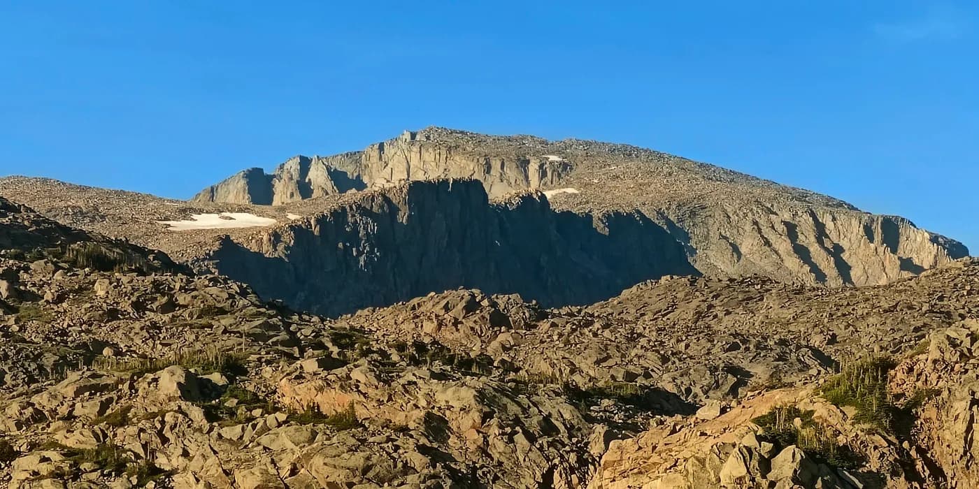 The broad sunlit granite face of Cloud Peak rises above rocky alpine talus under a clear blue sky.