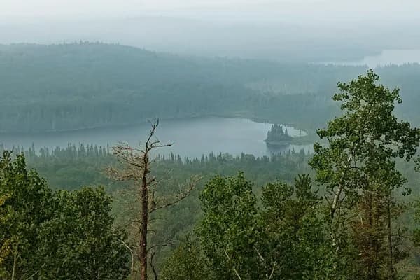 A hazy panorama from near Eagle Mountain across forested ridges and several lakes.