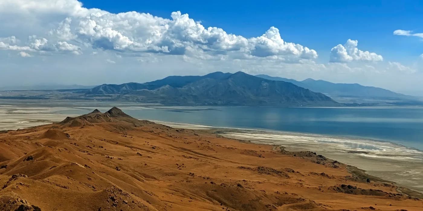 Dry ridges of Antelope Island descending toward the Great Salt Lake under a line of white clouds.