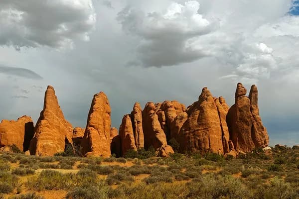 Cluster of orange sandstone pinnacles beneath dark grey and white storm clouds in Arches National Park.
