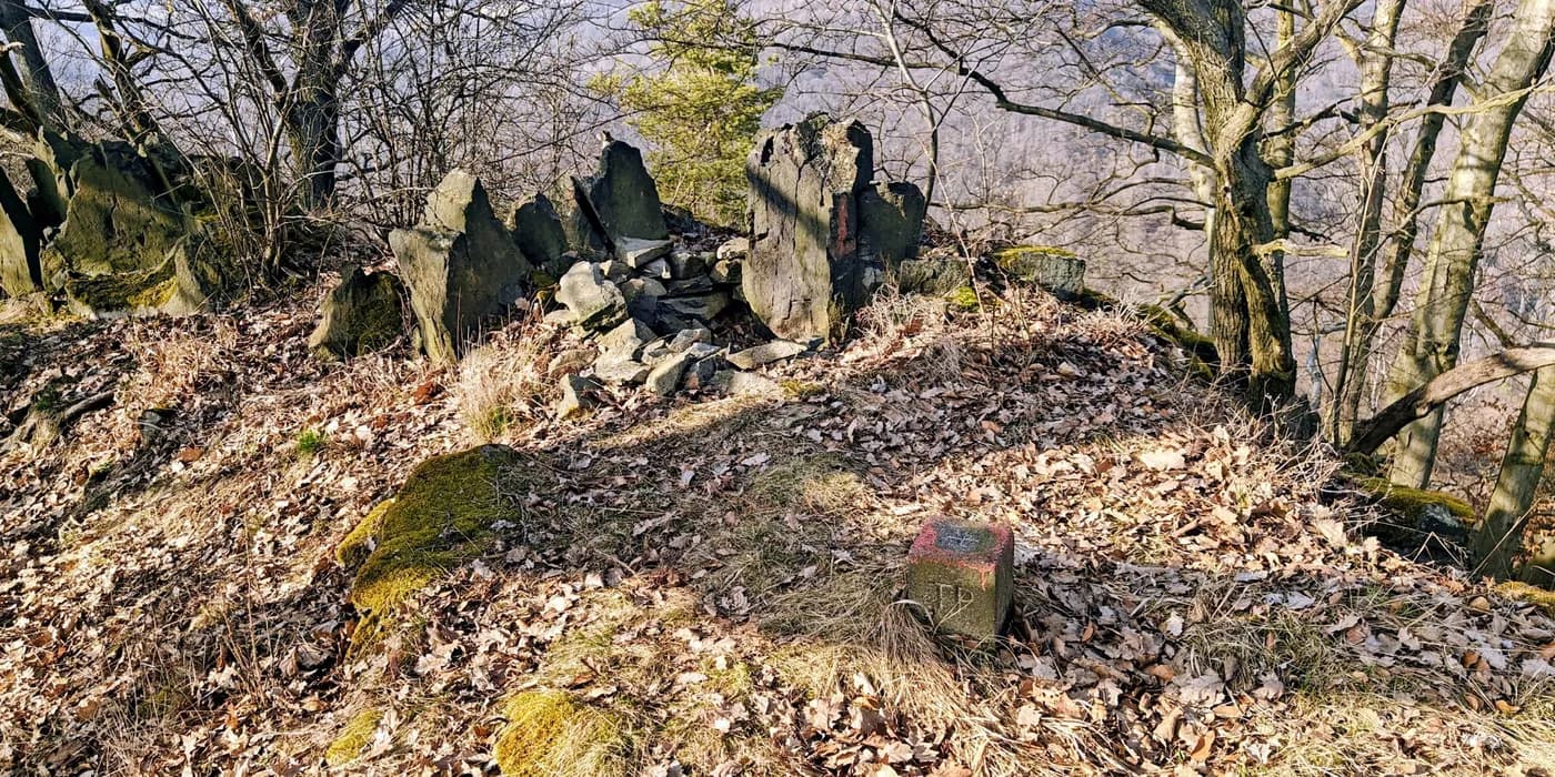 Rock outcrops and a small concrete marker on the leaf-covered wooded summit of Vysoký kámen.