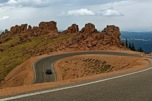 Car rounding a broad hairpin on Pikes Peak Highway through rocky alpine terrain beneath cloudy skies.