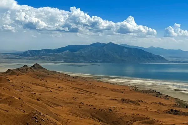 Dry ridges of Antelope Island descending toward the Great Salt Lake under a line of white clouds.