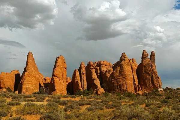 Cluster of orange sandstone pinnacles beneath dark grey and white storm clouds in Arches National Park.