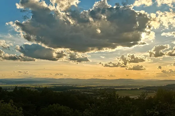 Late-afternoon view beneath dramatic clouds from the summit of Góra Świętego Jerzego above Strzegom.