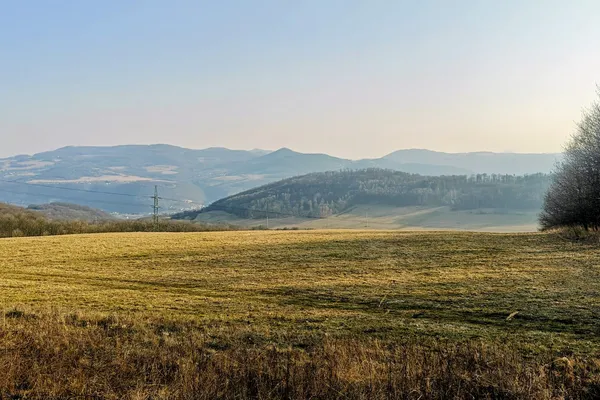 Late-afternoon sunlight across open fields and wooded hills below Radešín.