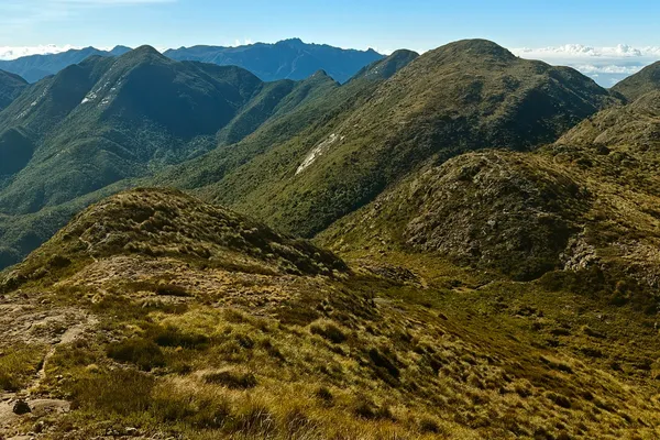 Long grassy and rocky ridge running through layered mountains under a clear blue sky.