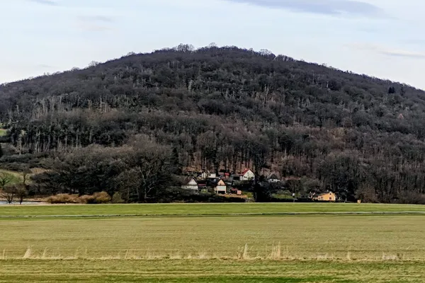 Wooded conical hill of Tuhošť rising above open fields and houses near Mezihoří.