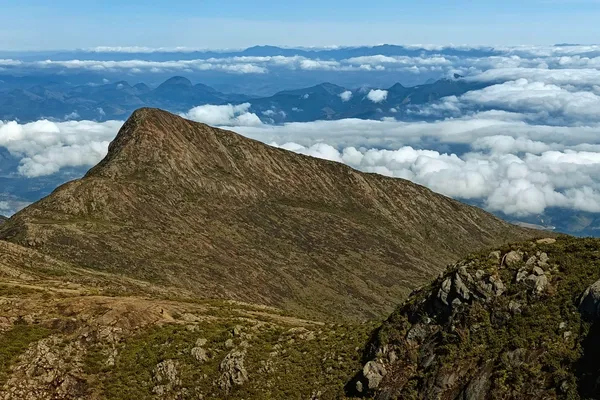 Rocky Caparaó ridge rising above a broad sea of clouds, seen from Pico da Bandeira.